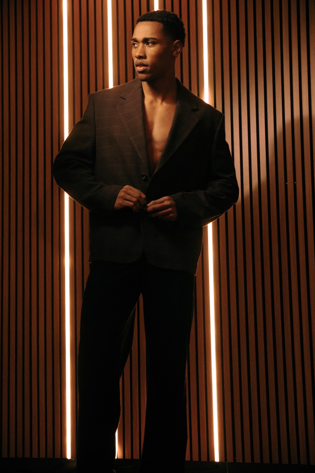 Model in brown suit against backlit wood slats