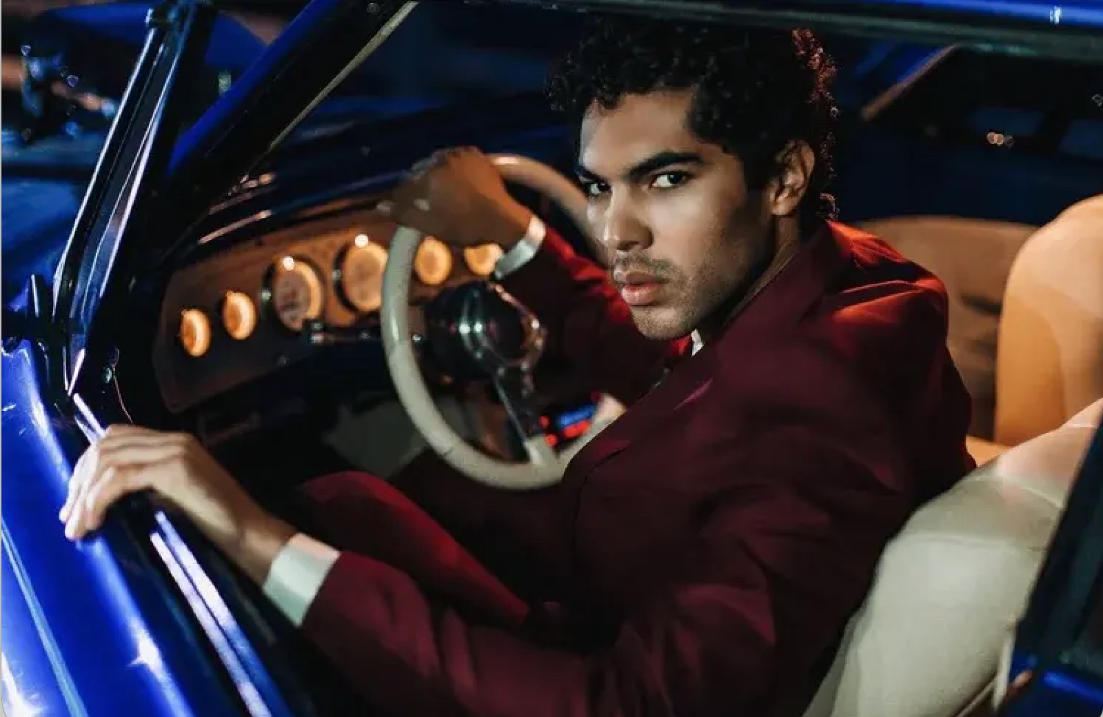Model in burgundy suit at the wheel of a vintage car